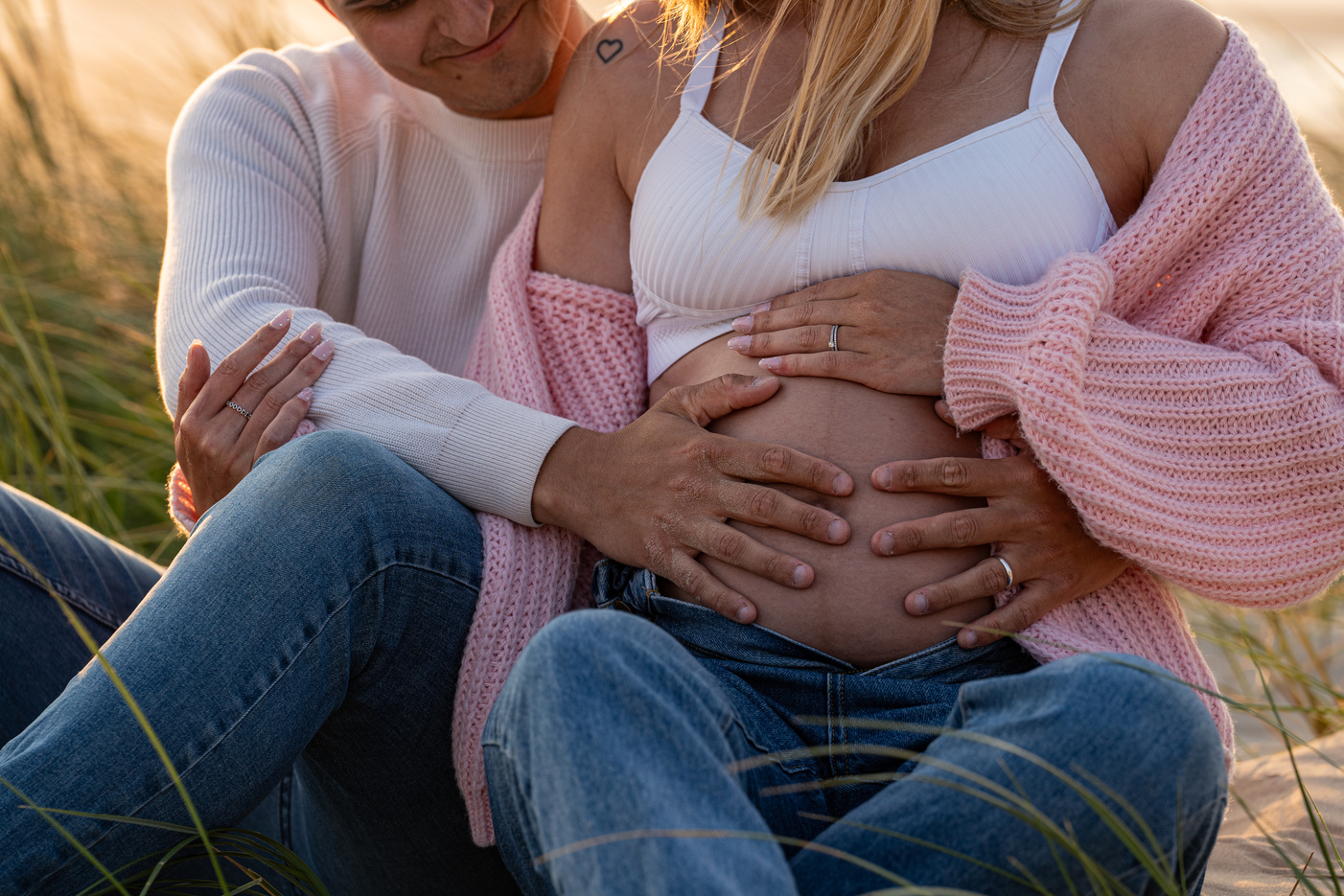 Grossesse, parentalité dans le nord de la France par Marine Derache photographe  représentant un couple de futurs parents tenant le ventre de la maman sur la plage de Dunkerque.